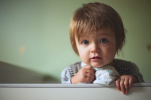 Toddler standing awake in bed holding blankie