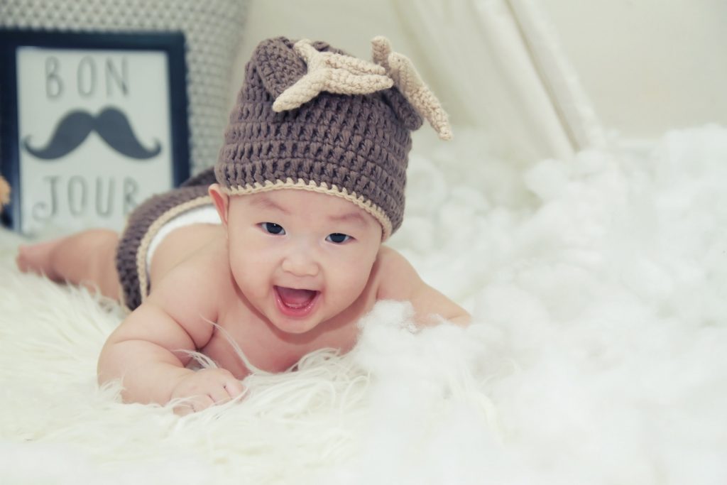 Adorable asian baby with beanie lying on furry carpet with bon jour sign