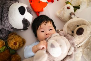 Asian baby boy covered and surrounded by teddy bears lying in bed