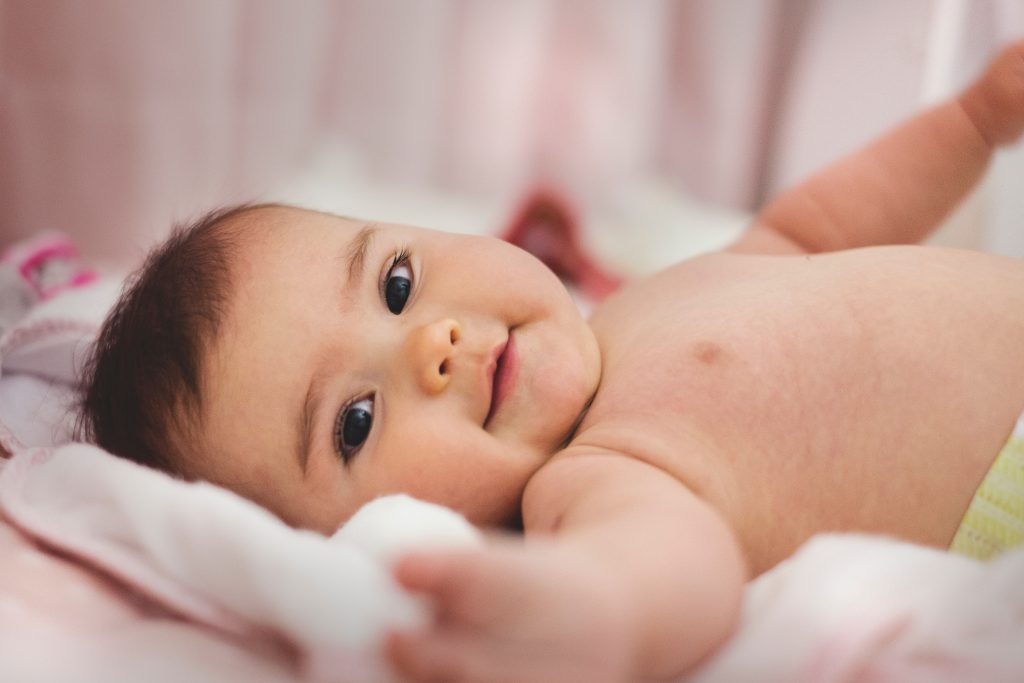 Beautiful baby girl lying on bed reaching out and smiling