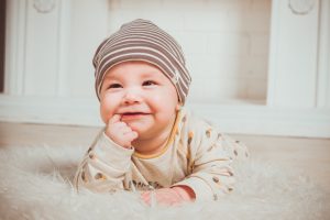 Adorable, happy baby boy having tummy time while chewing on his finger