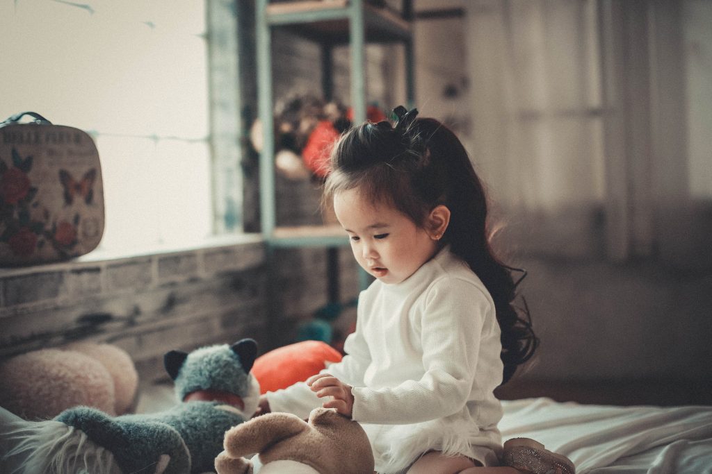 Beautiful asian toddler girl playing with stuffed animals on bed