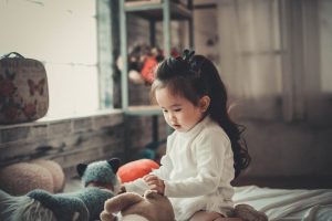 Beautiful asian toddler girl playing with stuffed animals on bed