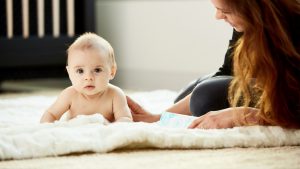 adorable baby on soft rug lying next to mom with crib behind them